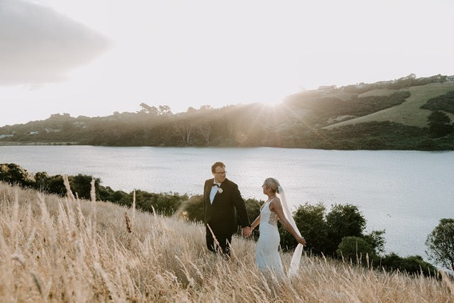 Wedding couple walking together in a field with a lake and mountains in the background.