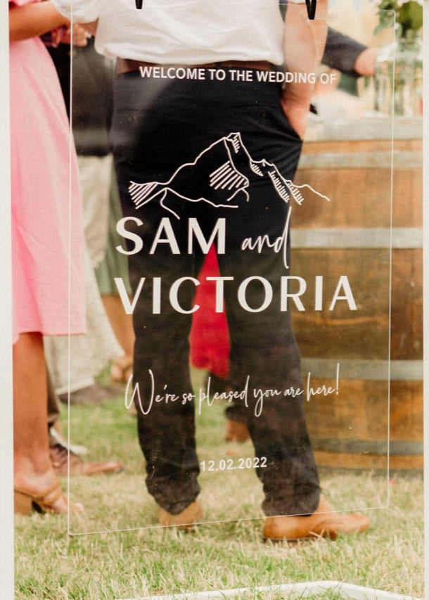 clear acrylic Wedding welcome sign with 'Sam and Victoria' at an outdoor event.