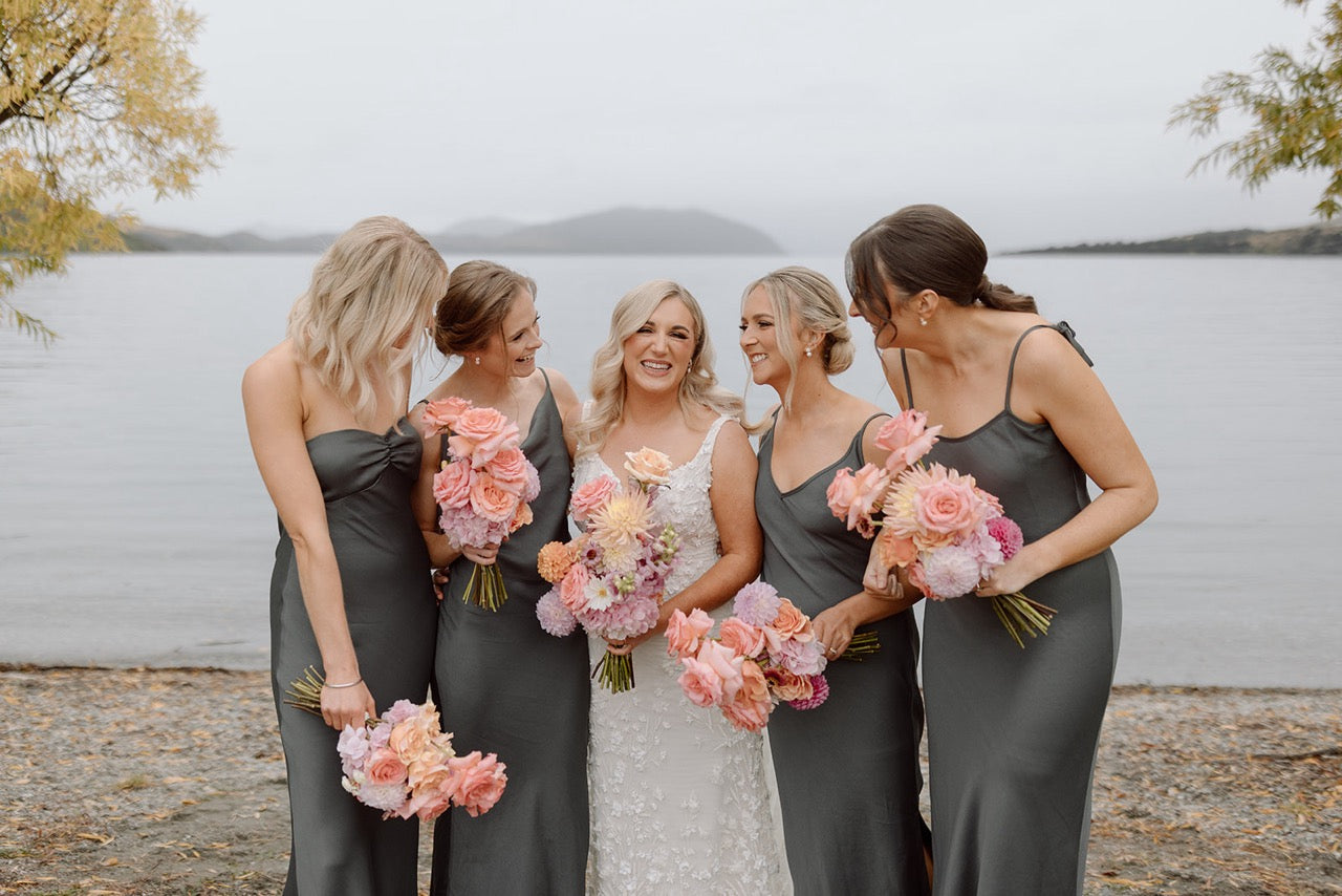 Group of women in gray dresses with floral bouquets by a lake wanaka