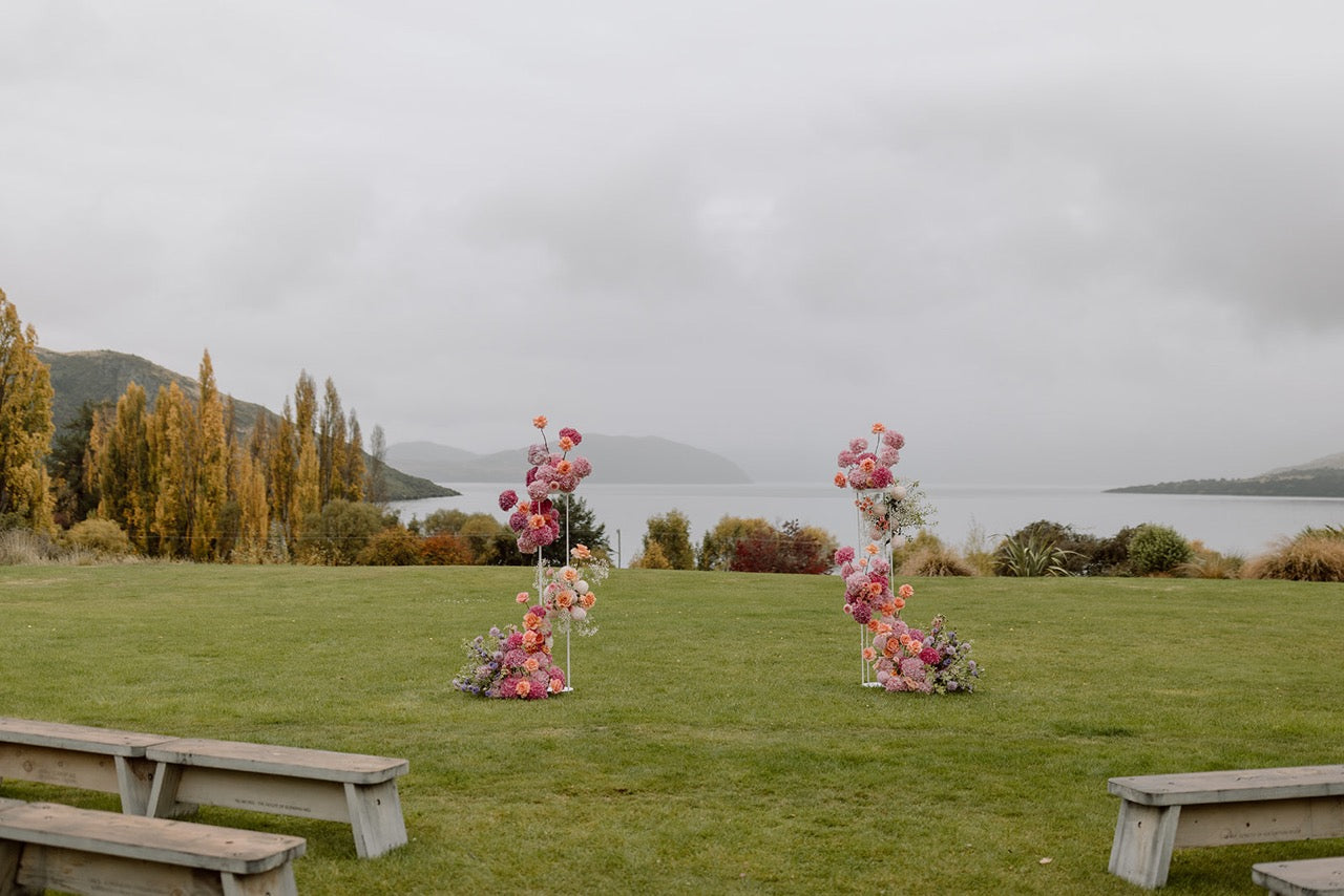 Floral arches on a grassy field with a lake and trees in the background at Glendhu Station