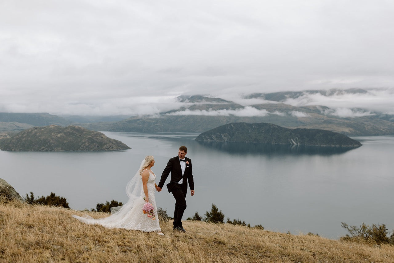 Wedding couple walking on a hill overlooking a lake with mountains in the background in wanaka