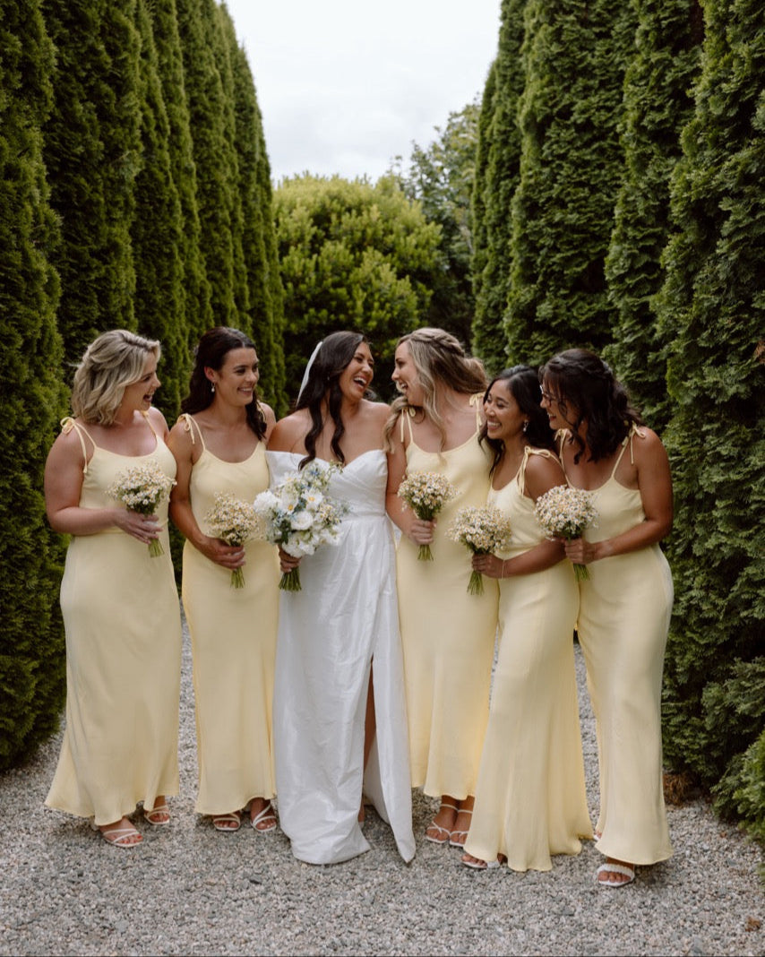 Bride in a white dress surrounded by bridesmaids in butter yellow dresses at The Winehouse Queenstown