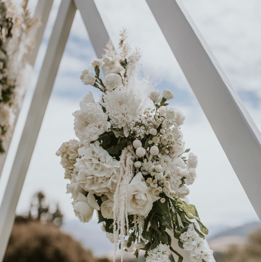 Decorative floral arrangement on a white archway with a blurred natural background