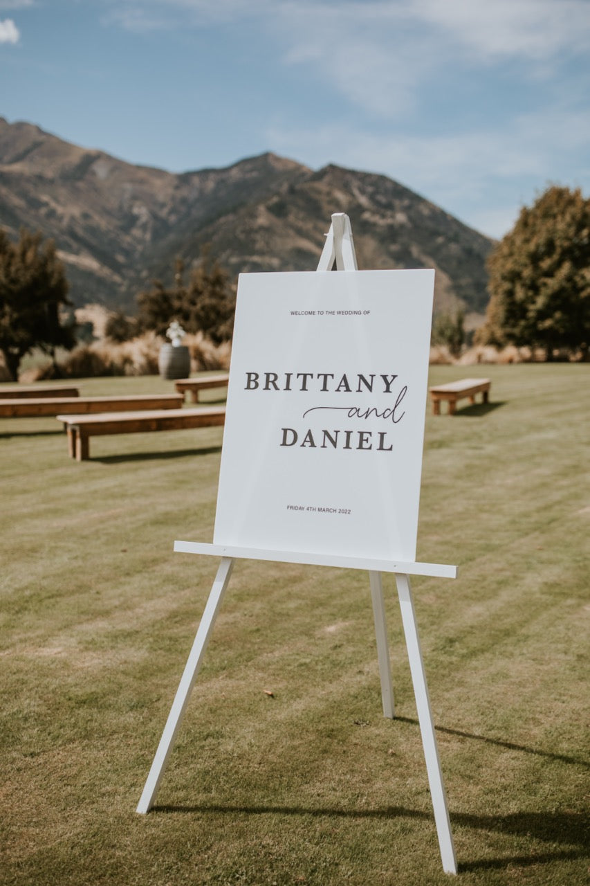 White sign with 'BRITTANY AND DANIEL' on an easel in a grassy outdoor setting with mountains at the Lookout Lodge Wanaka