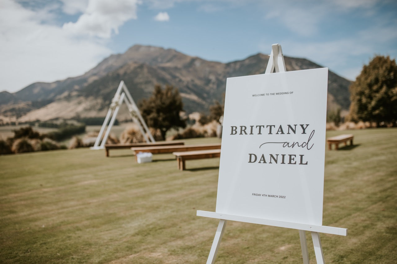 Wedding sign with 'Brittany and Daniel' on an easel in a scenic outdoor setting with mountains.