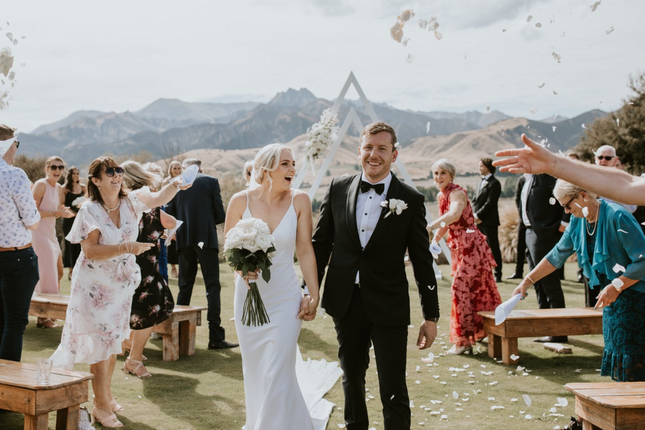 Wedding couple walking through confetti with guests on a mountainous background