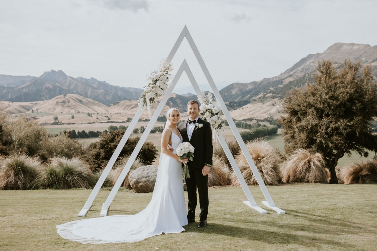 Couple standing under a triangle Archway with mountains in the background at the Lookout Lodge Wanaka