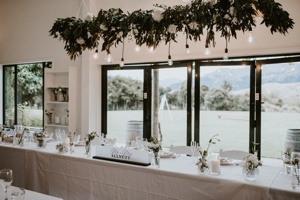 Decorated table with floral arrangements and a large floral installation above, set against a scenic window backdrop at the Lookout Lodge Wanaka