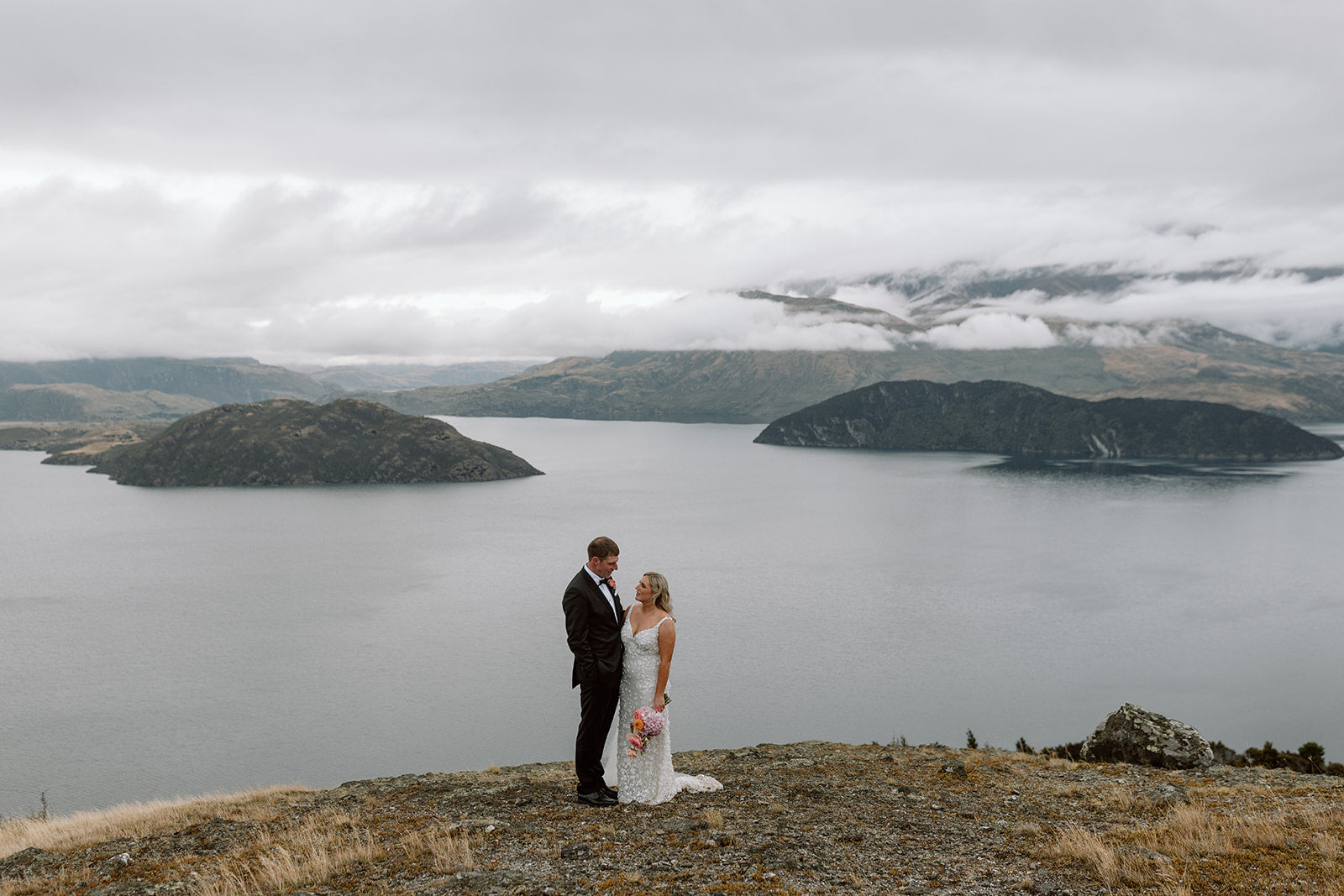 Couple standing on a cliff overlooking a lake with mountains in the background
