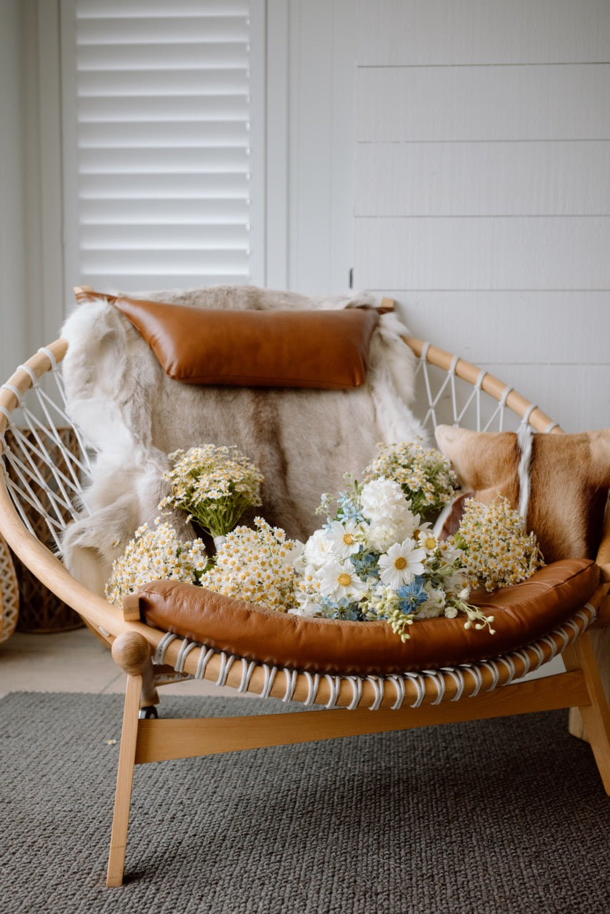 Wicker chair with flowers and a brown pillow against a white wall.