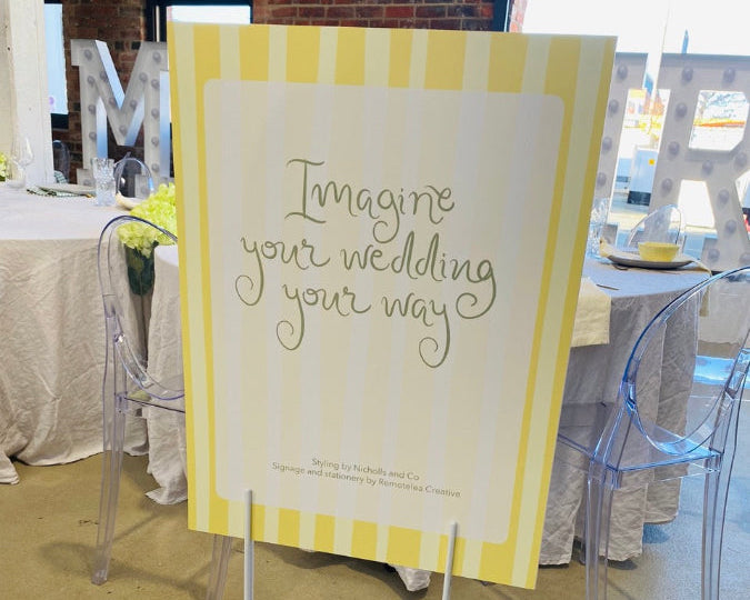 Yellow and white striped sign with 'Imagine your wedding your way set up at The Wedding Edit event in Dunedin