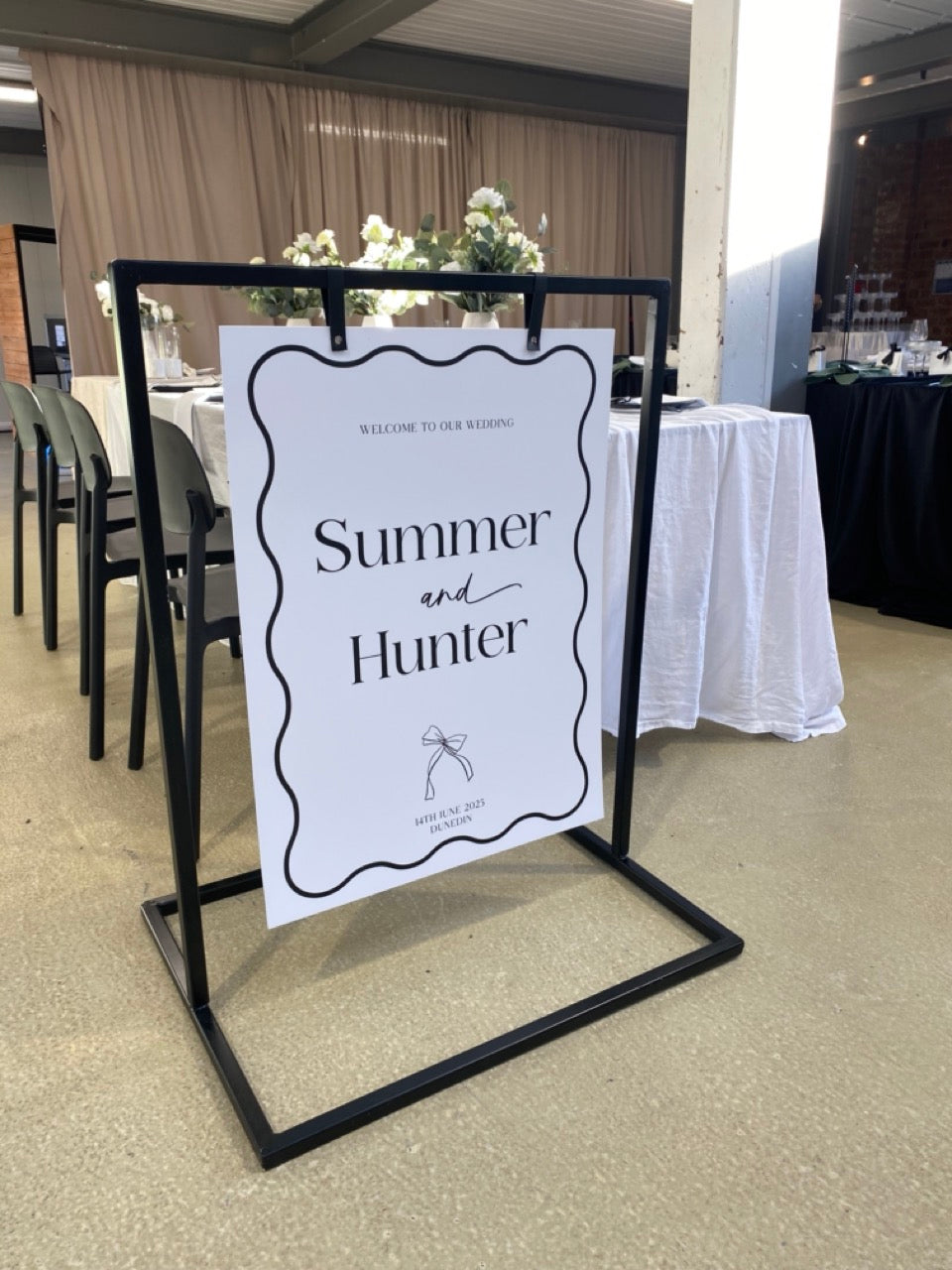 Black metal signage frame with a white welcome sign set up at The Wedding Edit event, Dunedin
