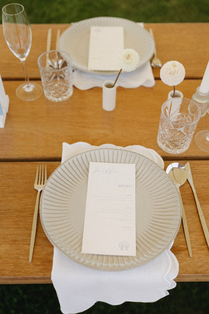 Elegant table setting with wedding menus, plates, glasses, and cutlery on a wooden table.