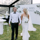 Wedding couple holding hands in front of a decorated backdrop with 'Mr & Mrs Marshall' text.