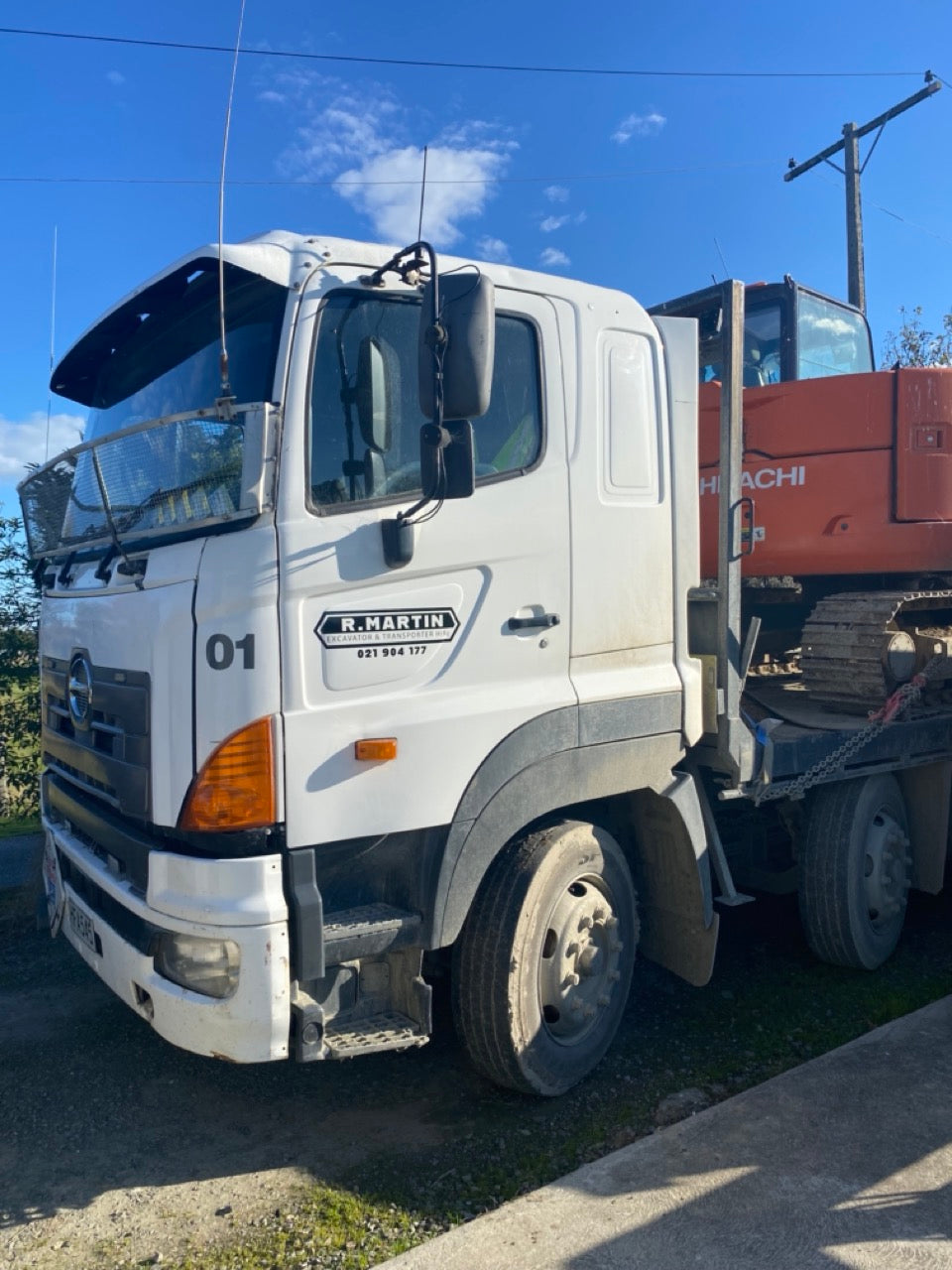 White truck with 'R. Martin' branding towing a red excavator on a clear day.