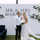 Wedding couple standing in front of a backdrop with 'MR & MRS MARSHALL' text.